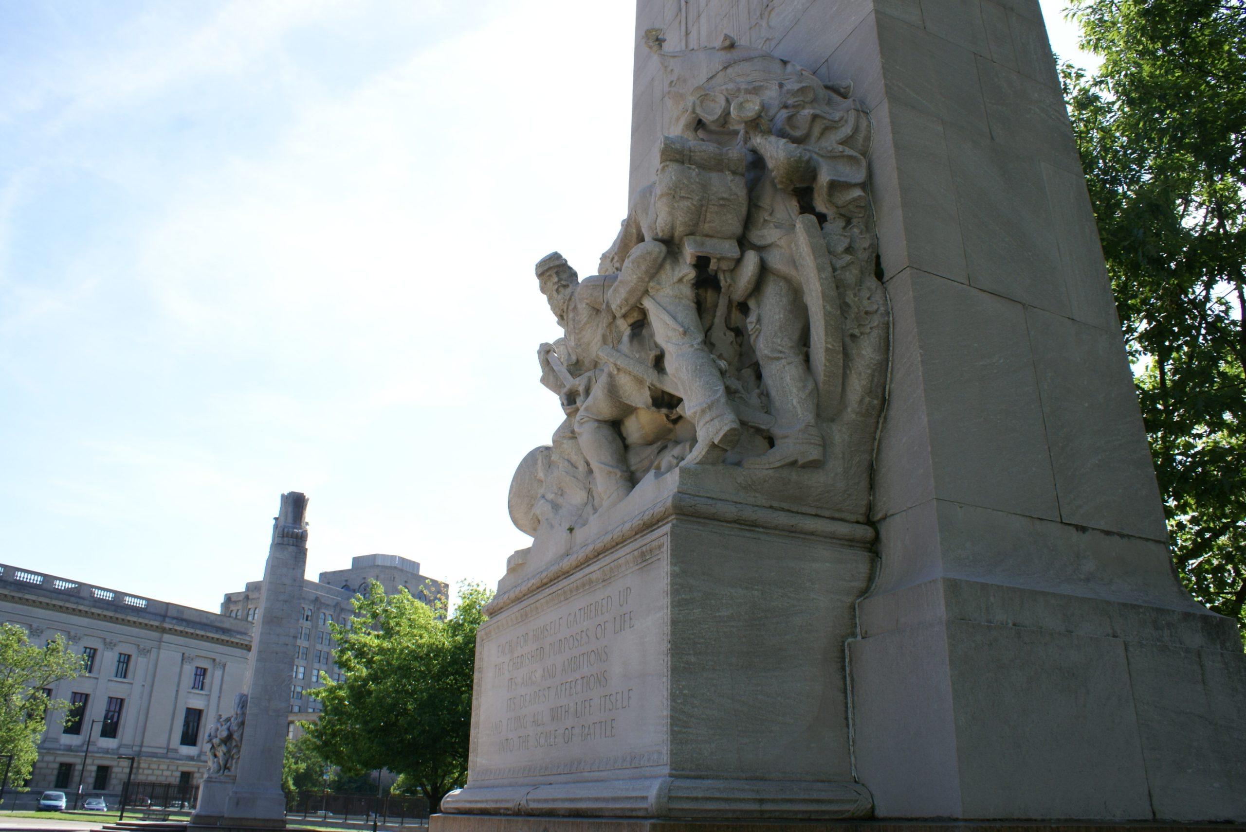 A high-relief stone carving on a public monument depicting a group of Civil War-era Union sailors and an officer with a cannon, framed by green trees.