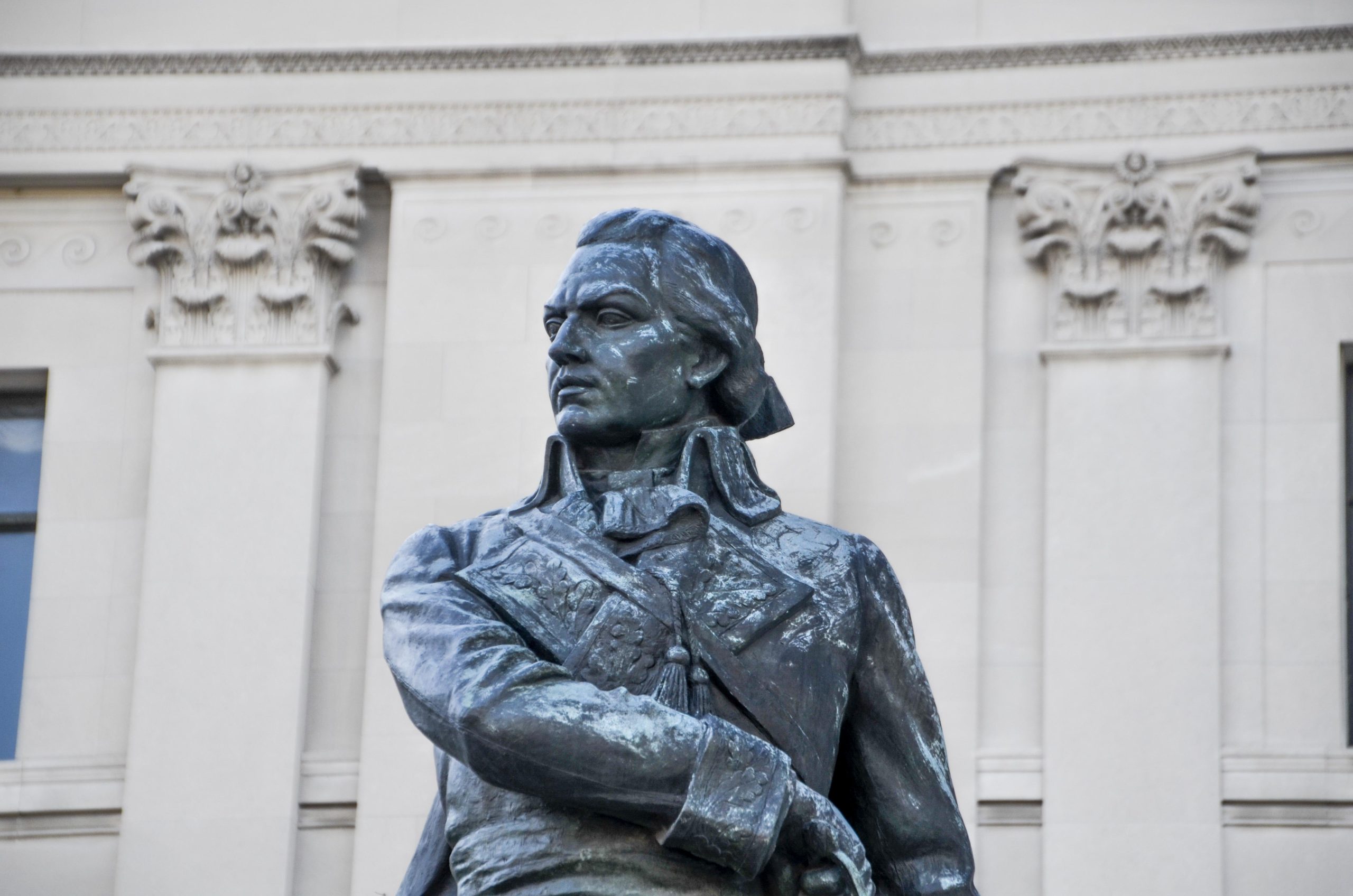 Detail shot of a bronze military statue in front of a neoclassical stone building.