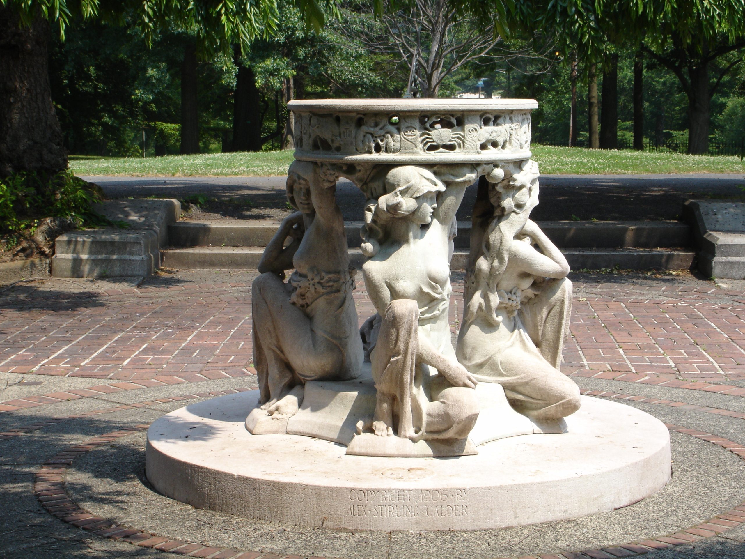 A marble sundial sculpture featuring female figures holding the sundial rimmed with zodiac figures.