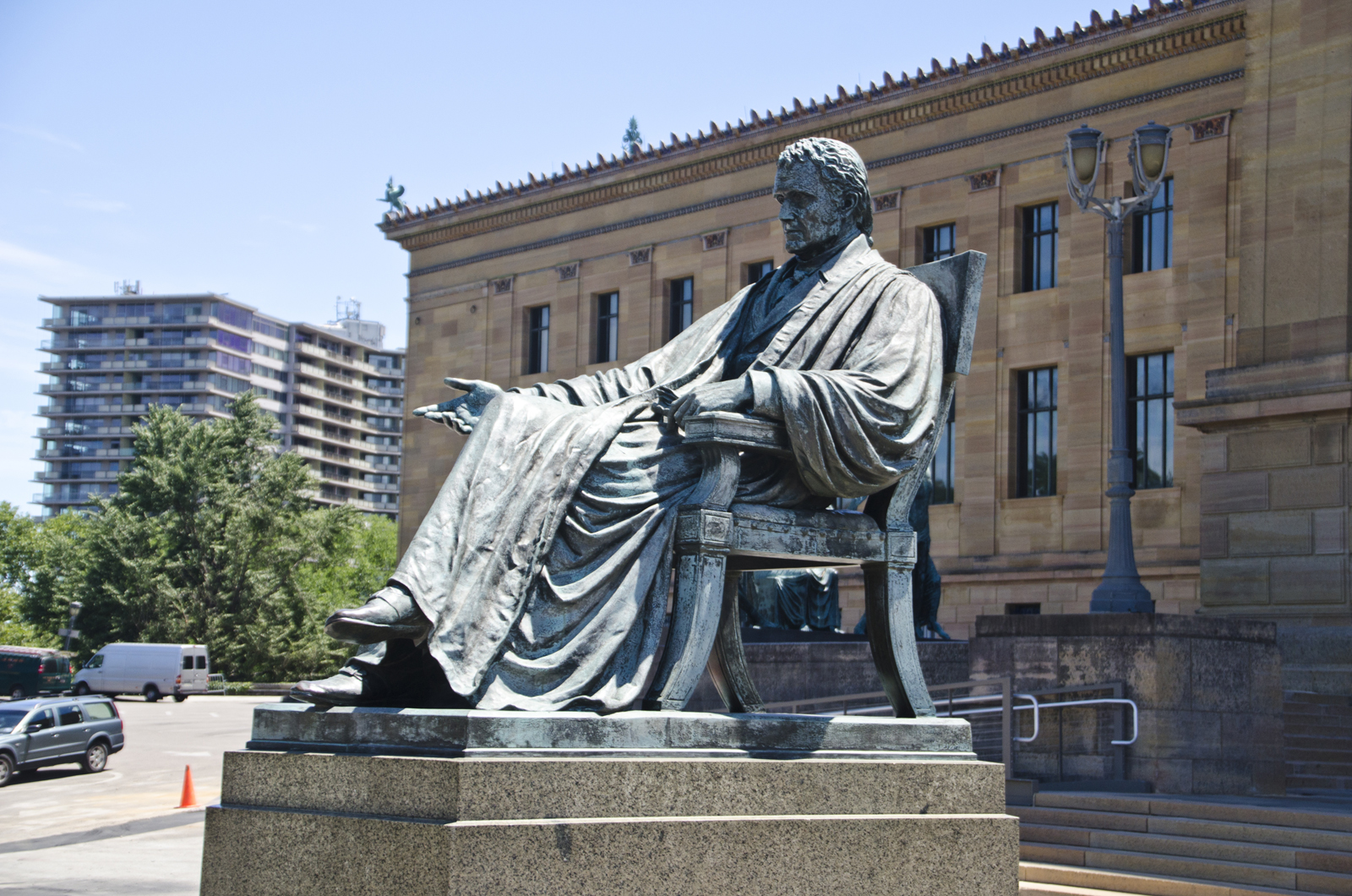 A weathered bronze sculpture of a seated judge behind a museum
