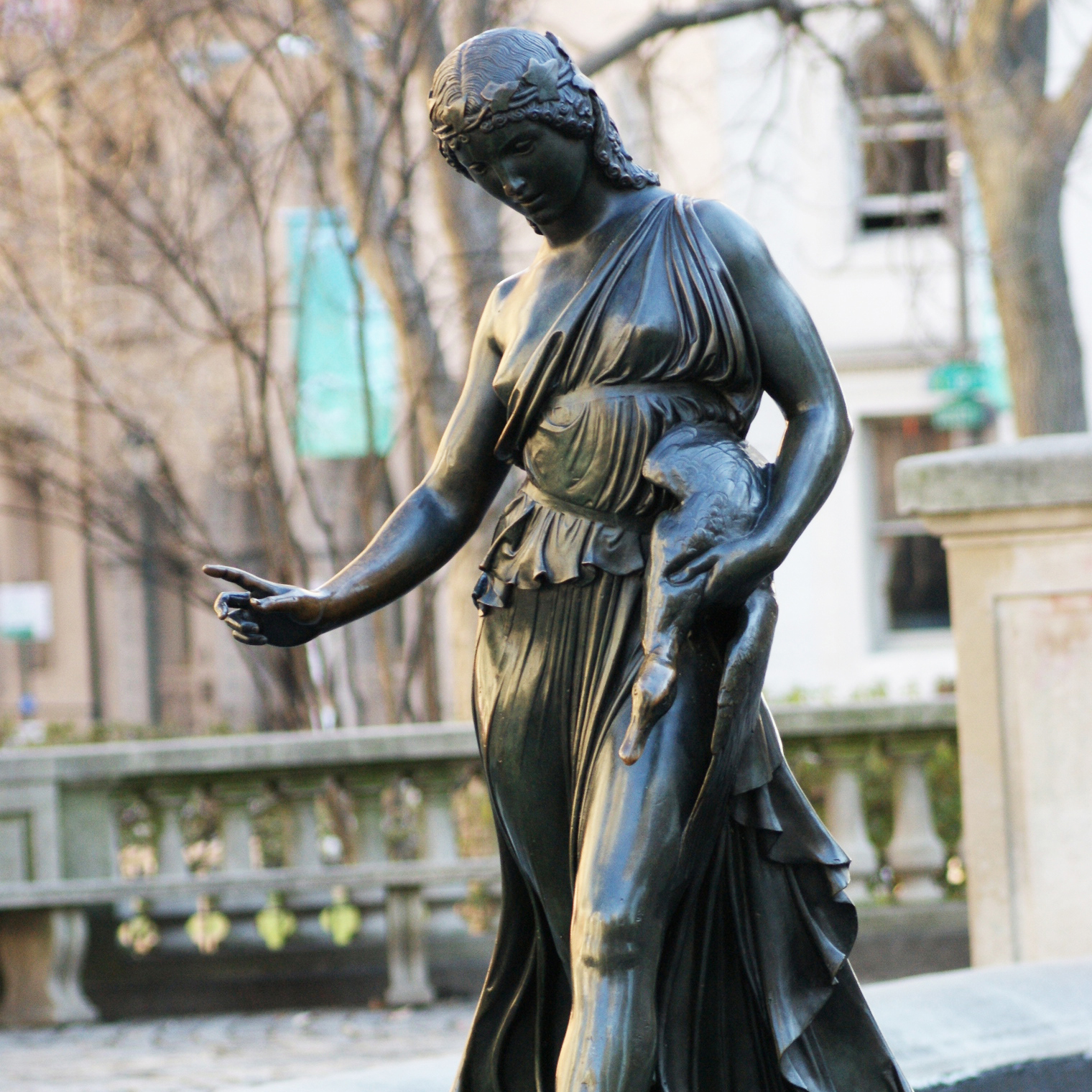 Bronze figurative statue of woman in a draped dress holding a duck with right hand held out and pointer finger pointing.